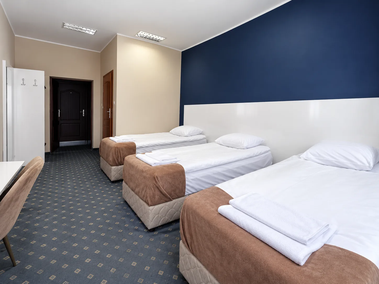 Pokój trzyosobowy comfort z trzema pojedynczymi łóżkami i granatową ścianą akcentową